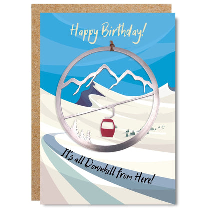 Gondola ornament placed on a birthday card illustrated with a picture of a mountain and written happy birthday, it's all downhill from here