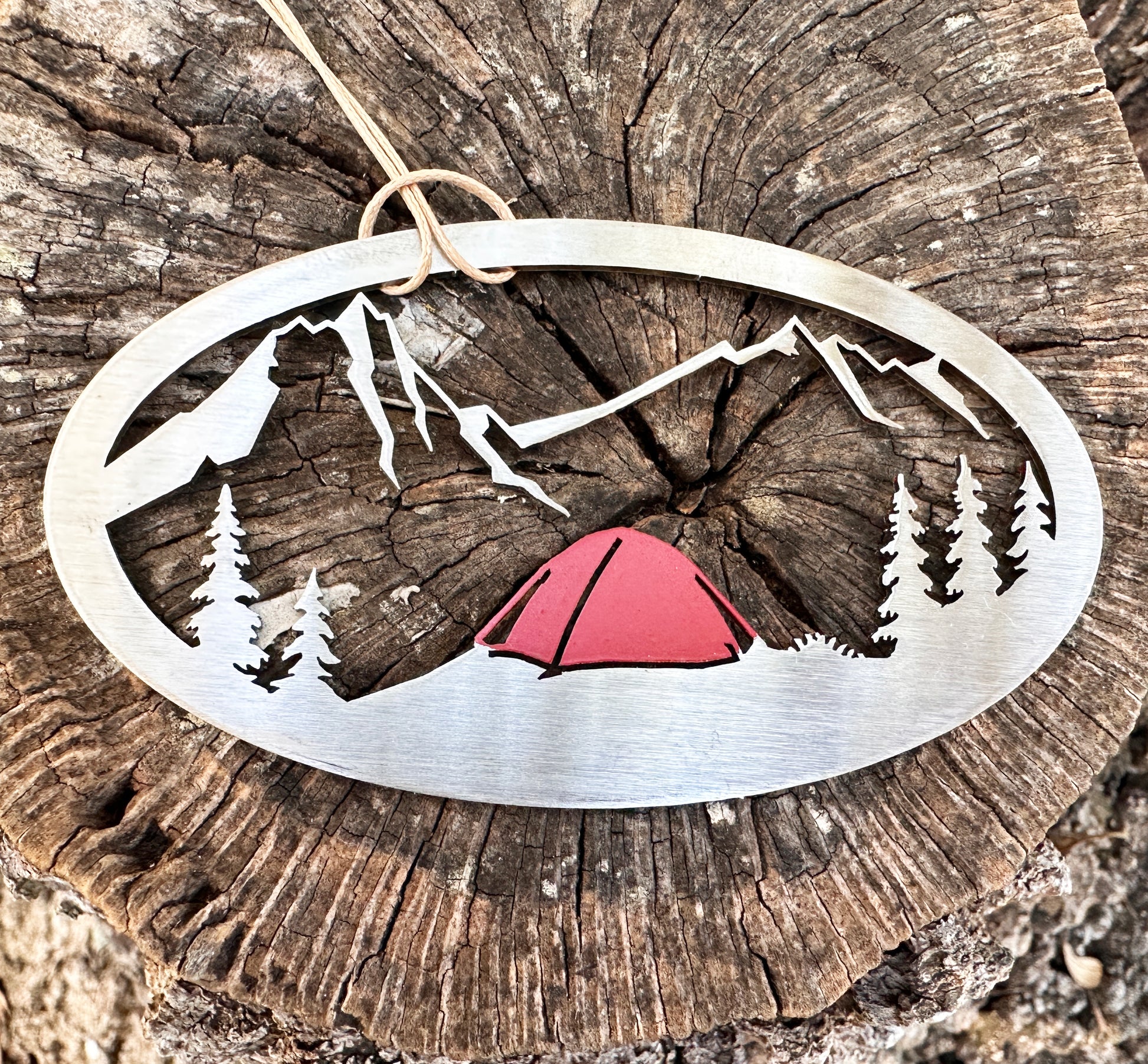 a metal ornament with a tent in the woods