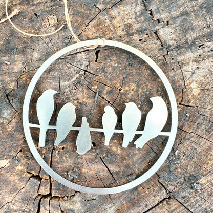 Circular shaped ornament, made of brushed stailnees steel and laser cut. Representing 6 birds on a wire, looking as if they are holding a comnversation. One of the bird, in the center, is upside down